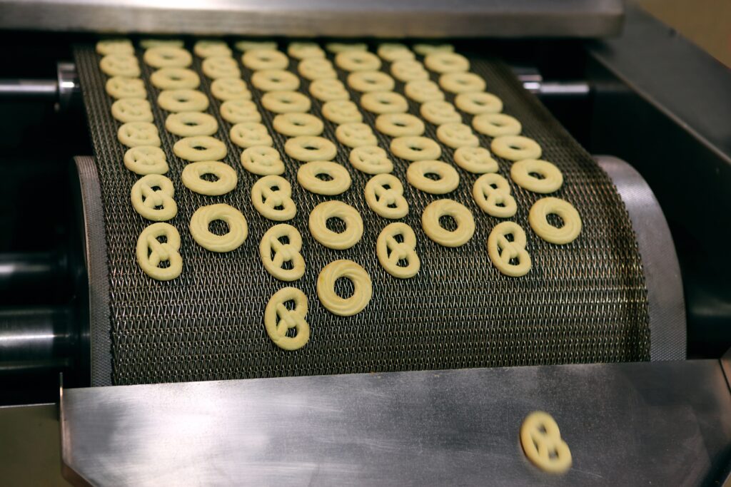 Pretzels lined up evenly in rows being transported along a food processing conveyor belt.