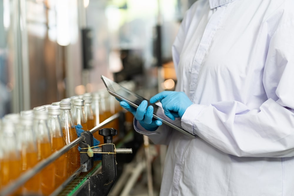 A worker assesses conveyor belt tracking and ensures drink bottles are moving smoothly.